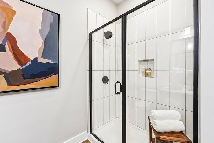 Modern bathroom with elegant glass shower, minimalist artwork, and neatly stacked towels on a wooden stool.