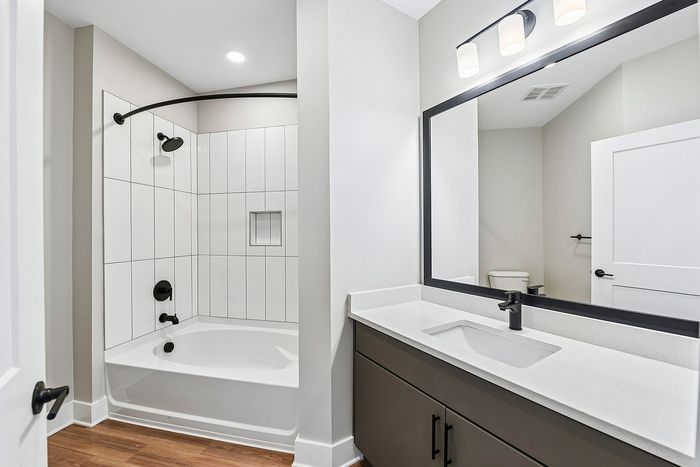 Modern bathroom with elegant white bathtub, sleek black fixtures, and spacious vanity under warm lighting.
