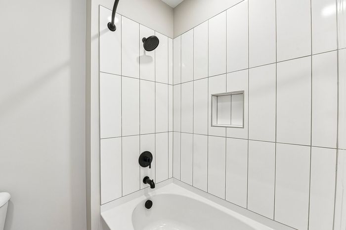 Elegant bathroom featuring sleek white tiles, modern black fixtures, and a stylish bathtub with built-in shelving.
