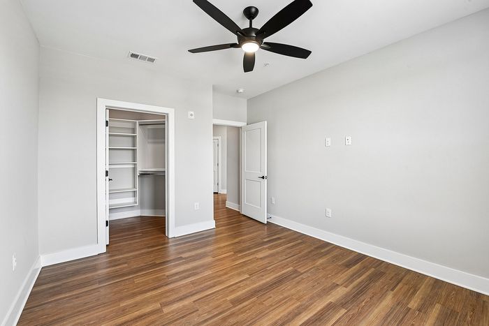 Bright bedroom with elegant wooden flooring, a sleek ceiling fan, and a walk-in closet, perfect for modern living.