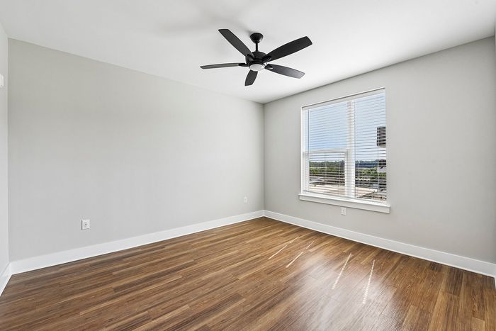 Bright, airy room with elegant wooden floors, modern ceiling fan, and large window offering scenic views.