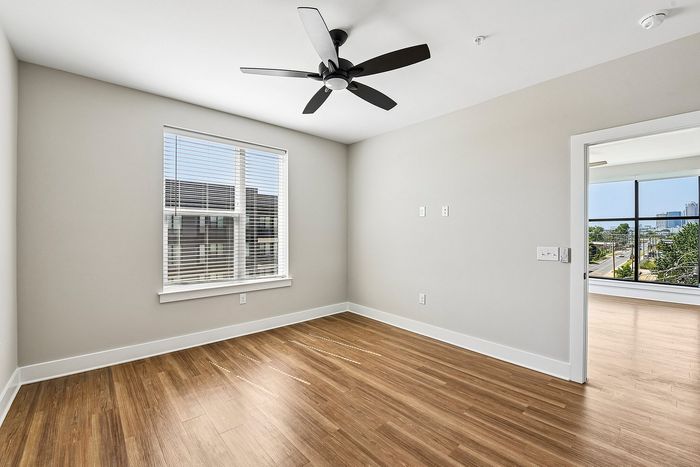 Modern bedroom with elegant hardwood flooring and a stylish ceiling fan, offering a bright and airy atmosphere with large windows providing scenic city views.