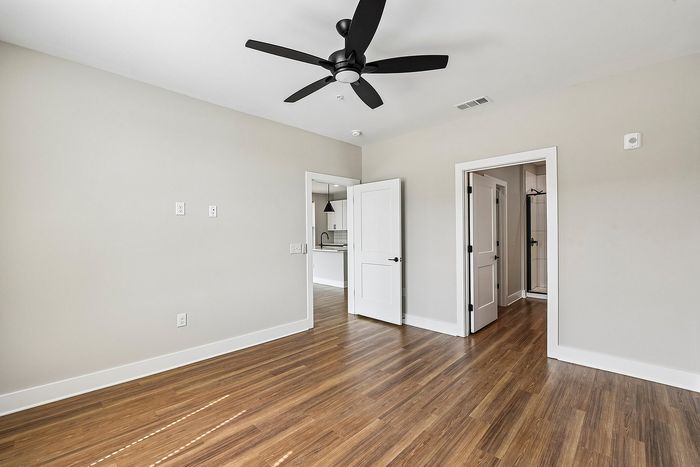 Modern apartment with elegant hardwood flooring, sleek ceiling fan, and open doorway views into a stylish kitchen.