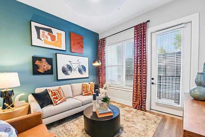 Chic living room with modern decor, featuring vibrant artwork, a cozy sofa with patterned cushions, and ample natural light through large windows.