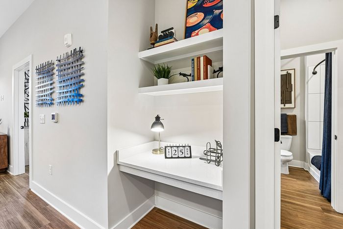 Charming home corner featuring a sleek white desk with artistic decor and a cozy, modern bathroom entrance, highlighting the warm wooden flooring.