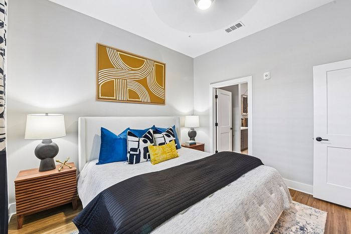Elegant bedroom with modern decor, featuring a cozy bed with vibrant pillows, stylish lamps on wooden nightstands, and contemporary wall art.