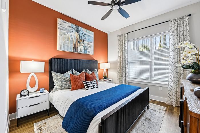 Inviting bedroom with vibrant orange accent wall, stylish artwork, and natural light illuminating cozy decor with plush pillows and modern furnishings.
