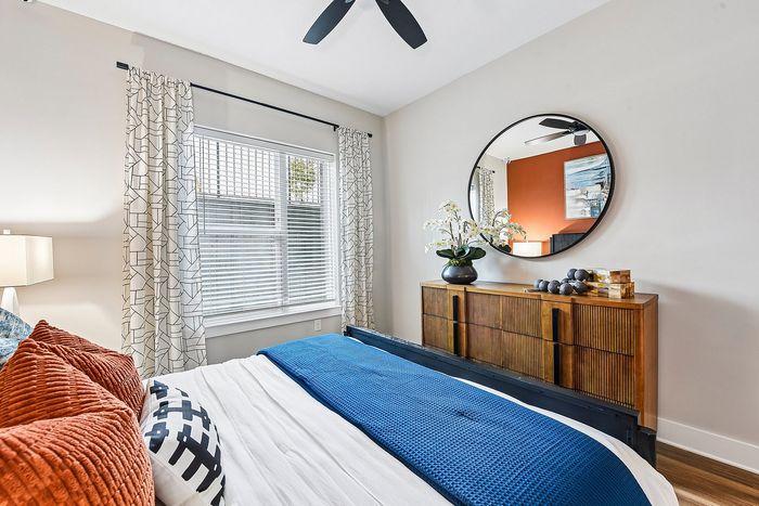 Bright and modern bedroom featuring a stylish wooden dresser, large mirror, and vibrant decor with plush pillows and a cozy blue throw.