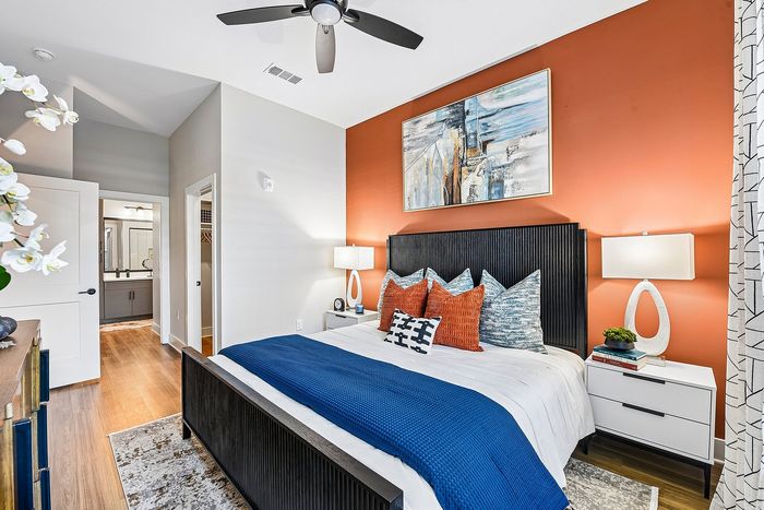 Modern bedroom with stylish orange accent wall, elegant decor, and cozy bedding, adjacent to a sleek en-suite bathroom.