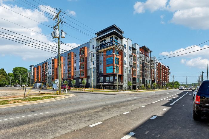 Modern multi-story apartment complex with vibrant facade, set along a wide street under a bright blue sky, ideal for urban living.