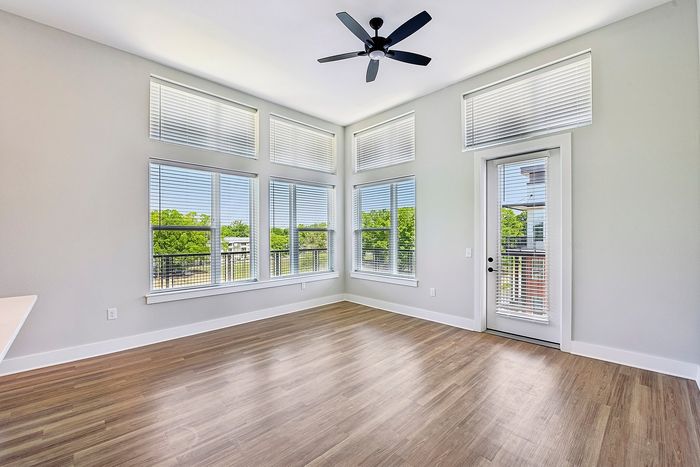 Bright living space with large windows, elegant wood flooring, and modern ceiling fan, offering a serene view of lush greenery.