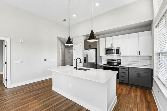 Modern kitchen with sleek white countertops, pendant lighting, and stainless steel appliances, featuring ample storage space and elegant wood flooring.