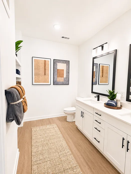 Modern bathroom featuring elegant white cabinets, stylish decor, and warm wood tone flooring, offering a serene and inviting atmosphere.