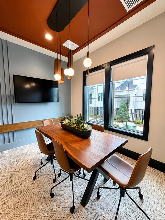 Chic meeting space with a modern wooden table, leather chairs, stylish pendant lighting, and natural accents in a bright room.