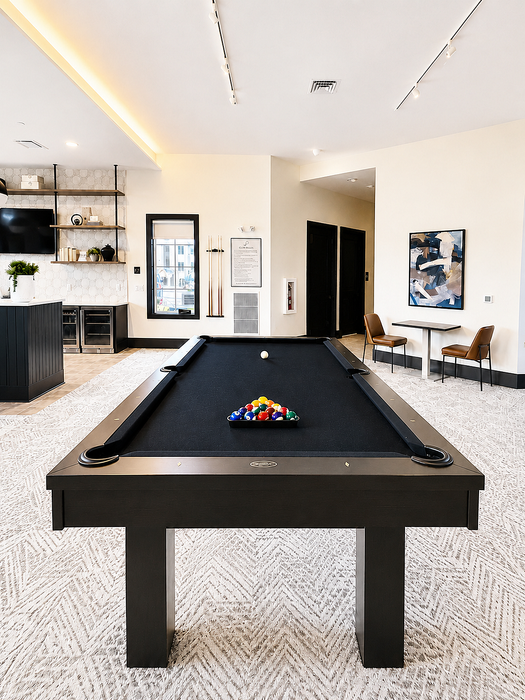Elegant recreation room featuring a sleek black pool table, chic modern decor, and a small seating area for relaxation.