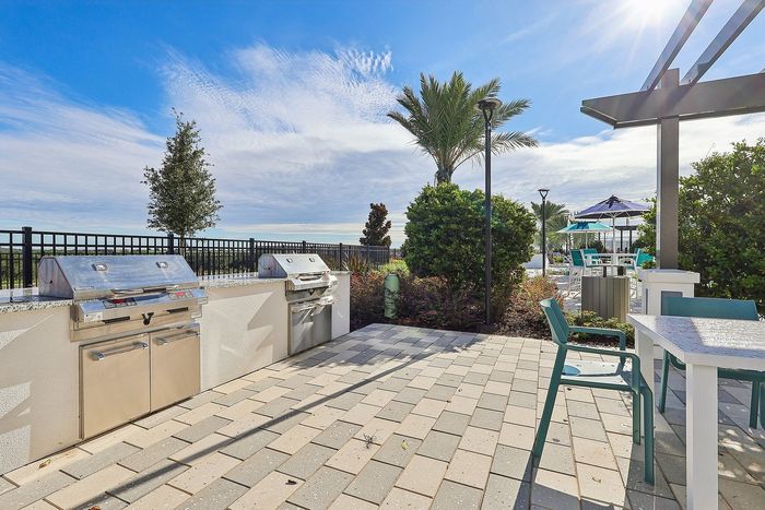 Sunny outdoor patio with modern grills and elegant seating, surrounded by lush landscaping and palm trees, perfect for entertaining.
