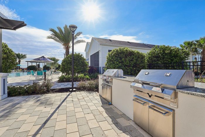 Luxurious outdoor area with stainless steel grills and a sparkling pool, surrounded by lush greenery and bright sunshine.