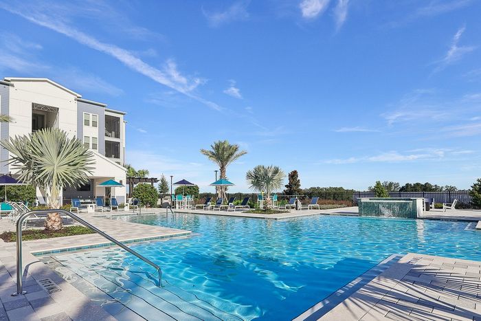 Luxurious outdoor pool area with palm trees and modern lounge chairs under a clear blue sky.