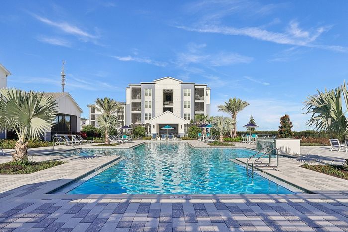 Luxurious apartment complex with a stunning outdoor pool, surrounded by palm trees and contemporary architecture under a clear blue sky.