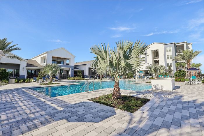 Luxurious apartment complex featuring a resort-style pool surrounded by lush palm trees and sun loungers, offering a perfect tropical escape.