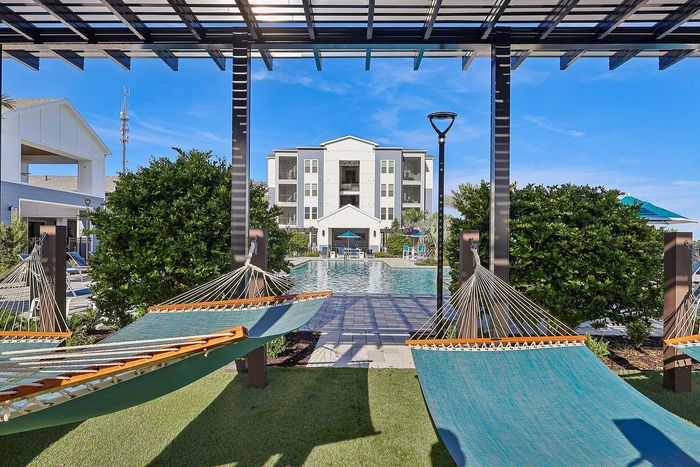 Luxurious apartment complex with modern architecture, featuring serene poolside hammocks under a stylish pergola, perfect for relaxation and leisure.