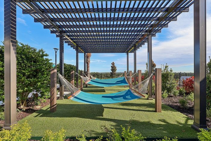 Serene outdoor escape featuring shaded pergolas with vibrant blue hammocks, surrounded by lush greenery and open skies.