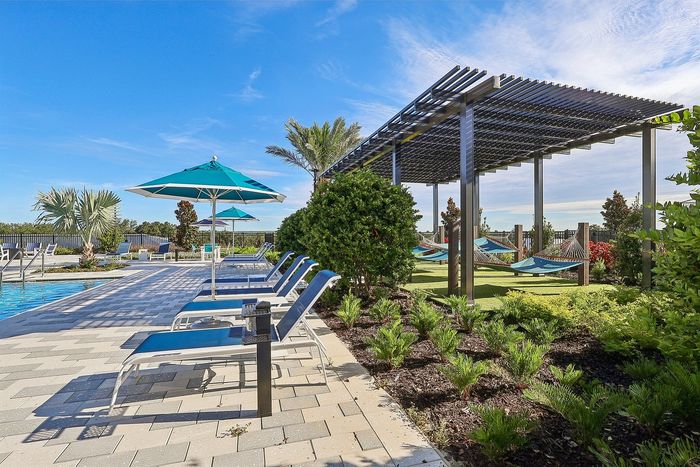 Luxurious outdoor pool area with stylish loungers, vibrant umbrellas, and relaxing hammocks by lush greenery and blue skies.