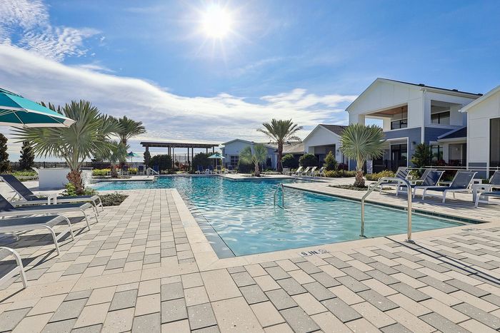 Luxurious apartment complex with a stunning sunlit outdoor pool area, surrounded by palm trees and modern loungers, offering a resort-like experience.