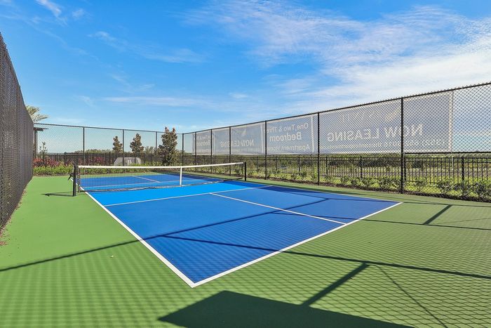 Vibrant outdoor tennis court surrounded by lush greenery and bright blue skies, perfect for leisure and sports enthusiasts.