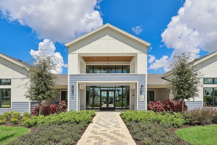 Inviting modern building facade with a grand entrance, lush landscaping, and bright skies.