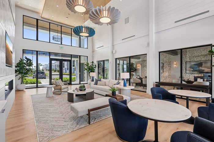 Luxurious modern lounge area with high ceilings, elegant seating, chic lighting fixtures, and expansive windows offering natural light and garden views.