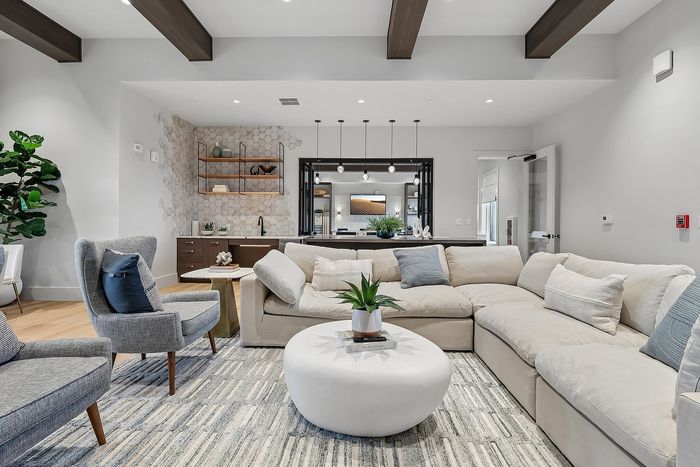 Chic modern living room featuring a plush L-shaped sofa, elegant armchairs, and a stylish round coffee table, seamlessly blending with an open kitchen adorned with geometric wall tiles and contemporary lighting.