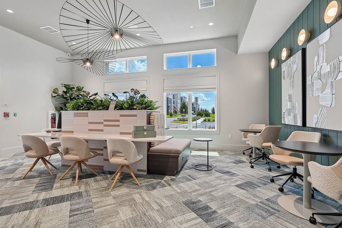 Modern and inviting communal workspace with stylish chairs, sleek tables, and vibrant planters under artistic ceiling lights.