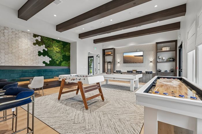 Modern recreation room featuring sleek pool and foosball tables, vibrant green living wall art, and stylish blue seating for an inviting entertainment space.
