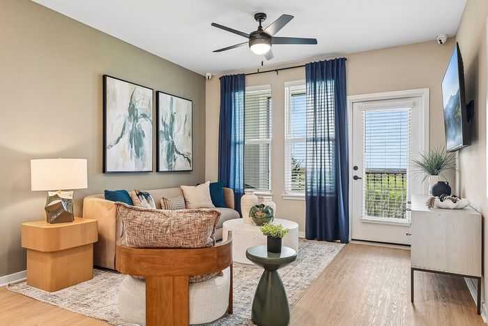 Charming living room with modern decor, featuring a plush couch, abstract artwork, and large windows draped with elegant curtains.