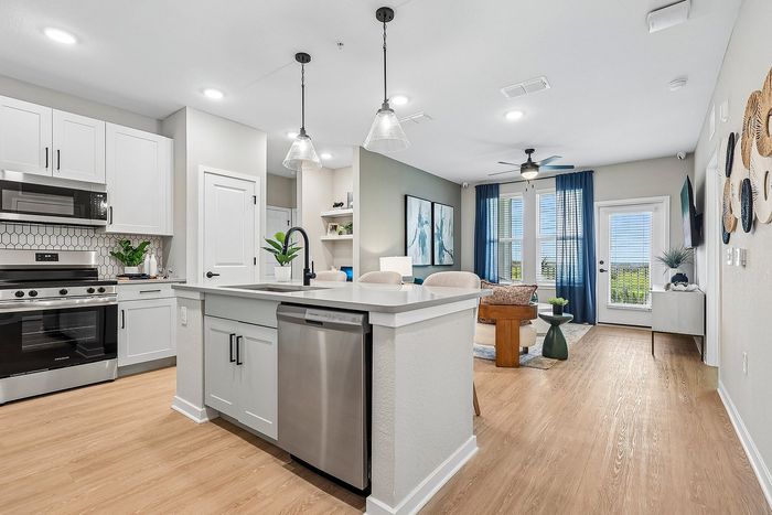 Modern open-plan kitchen featuring sleek white cabinetry, stainless steel appliances, and a cozy living area with large windows and stylish decor.