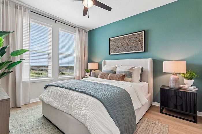 Inviting bedroom with a luxurious bed, stylish teal accent wall, elegant decor, and large windows offering serene views.