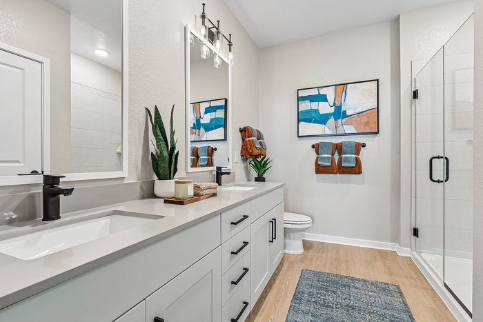 Bright and modern bathroom featuring sleek dual sinks, stylish black fixtures, chic artwork, and a spacious glass-enclosed shower.