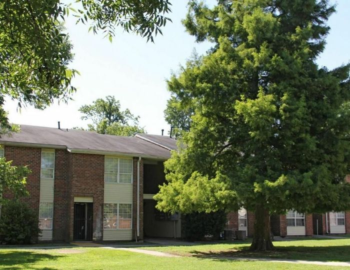 Charming red-brick apartment complex surrounded by lush green lawns and mature trees, offering a serene living environment.