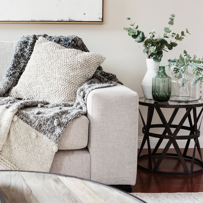 Inviting living room corner with a cozy beige sofa, textured pillows, and a chic side table accented by vibrant greenery.