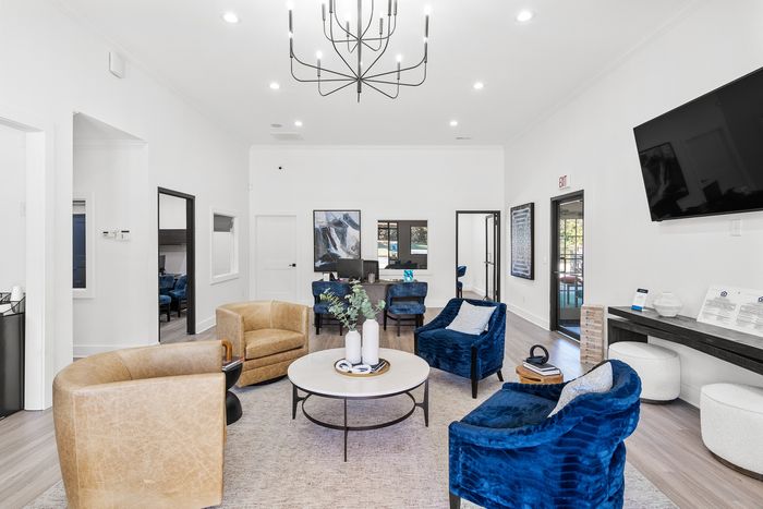 Modern and inviting living space showcasing elegant blue velvet chairs, cozy tan armchairs, and tasteful decor under a chic chandelier.