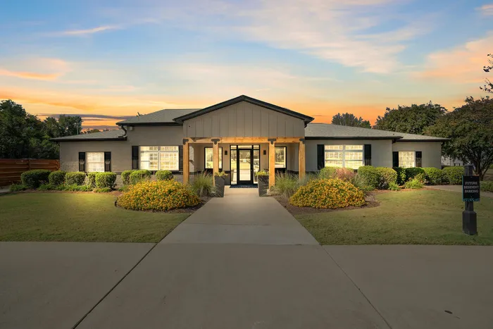 Welcoming entryway of a modern residence surrounded by lush landscaping and a picturesque sunset sky.