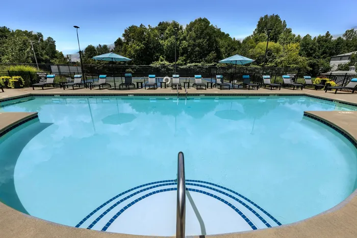 Inviting outdoor pool area with crystal-clear water, surrounded by lush greenery and stylish lounge chairs under blue umbrellas.