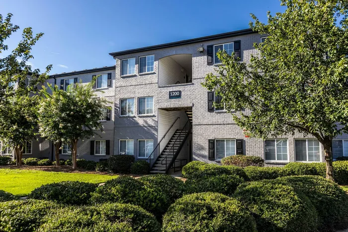 Charming apartment building with modern gray brick facade, sunlit windows, and lush green landscaping.