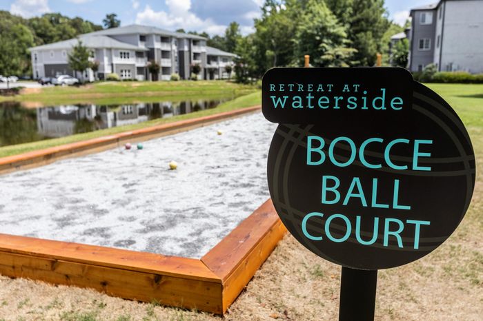 Charming community bocce ball court at Retreat at Waterside with serene pond views and modern apartment buildings in the background.
