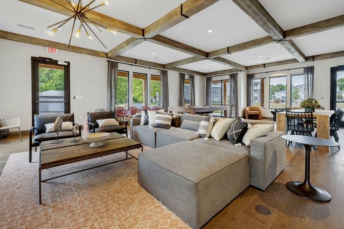 Elegant apartment lounge with modern wooden beams, cozy seating, stylish decor, large windows, and abundant natural light.