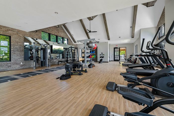 Spacious and modern gym featuring top-of-the-line fitness equipment, bright natural light, and stylish exposed brick walls.