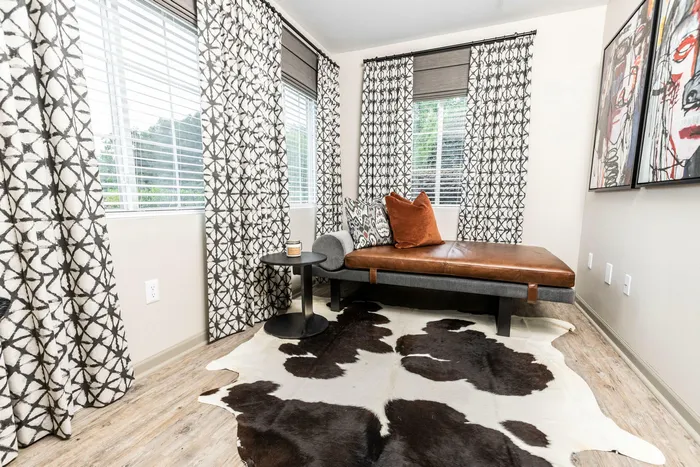 Chic apartment with stylish lounge featuring a sleek leather daybed, patterned throw pillows, abstract artwork, and a cowhide rug under cozy natural light.