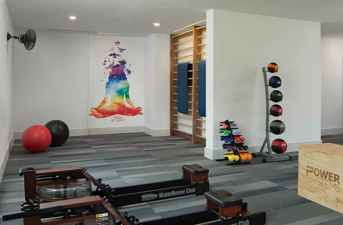 Modern yoga studio featuring vibrant wall art, exercise equipment, and a sleek rowing machine, creating an inviting fitness space.