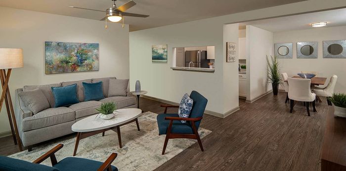 Modern open-concept living and dining area with stylish furniture and elegant decor, featuring a cozy gray sofa, vibrant artwork, and a sleek dining table with plush chairs.